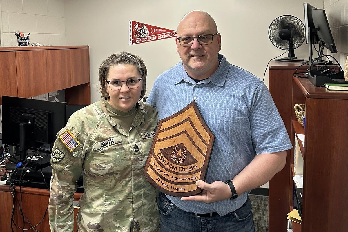 A retiring command sergeant major holding an engraved wooden plaque presented by an EANGKY officer